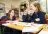 Two school children sitting at a desk doing a mindfulness activity, with a teacher crouched down beside their desk.