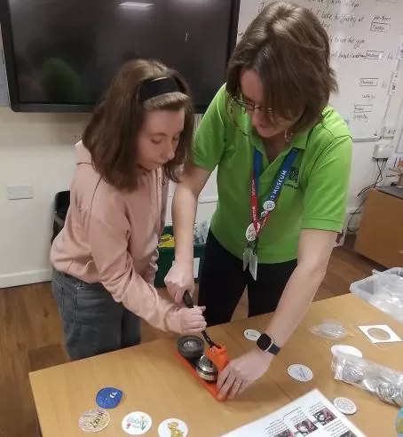An adult standing beside a young person, helping them with a craft activity on a table.