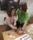 An adult standing beside a young person, helping them with a craft activity on a table.