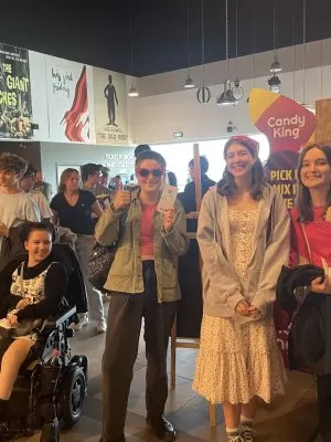 Five young people standing and one young person in a wheelchair, in a cinema, facing the camera and smiling.