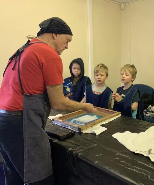 A teacher with four children demonstrating how to do screen printing.