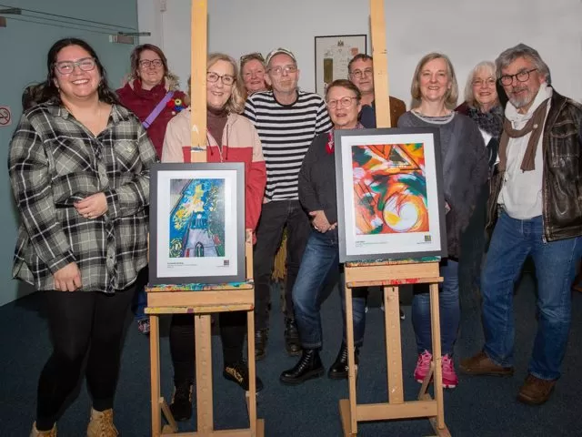 People gathered around two pieces of art on easels. They are all facing the camera.