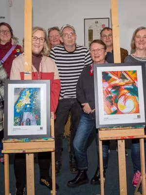 People gathered around two pieces of art on easels. They are all facing the camera.