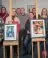 People gathered around two pieces of art on easels. They are all facing the camera.