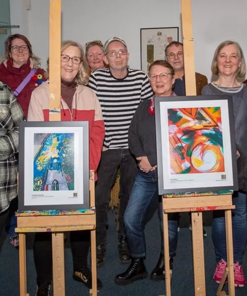 People gathered around two pieces of art on easels. They are all facing the camera.