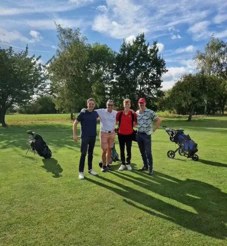 Four people standing huddled together facing the camera at a golf course.