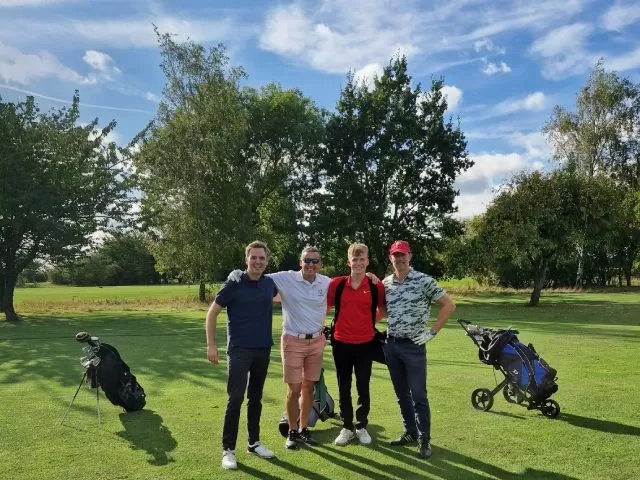 Four people standing huddled together facing the camera at a golf course.