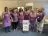 6 ladies in purple tops or aprons standing around a white food pantry sign.