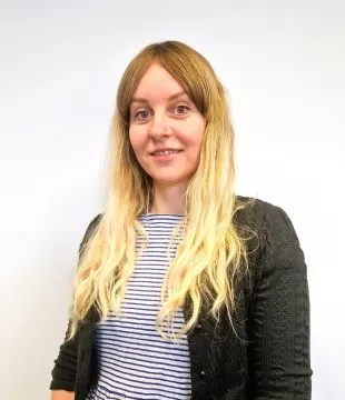 Headshot of Sara Marshall in a striped black and white top and black cardigan. She is standing in front of a white background.