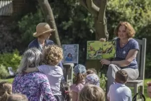 Children and their carers facing two people reading stories from books.