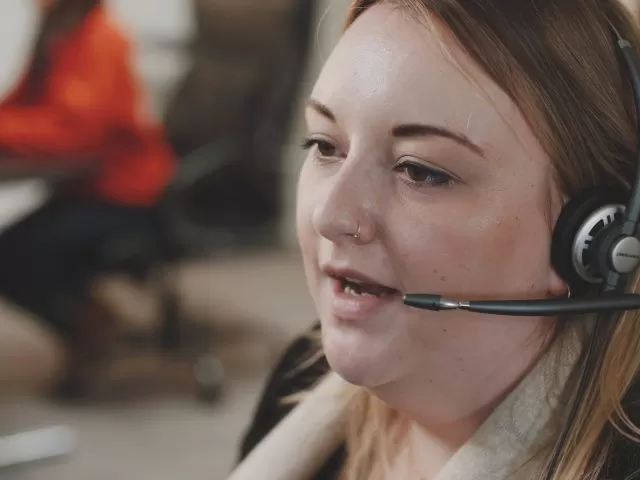 A close up shot of a helpline advisor mid-call, wearing a headset.