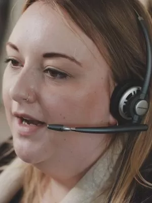 A close up shot of a helpline advisor mid-call, wearing a headset.