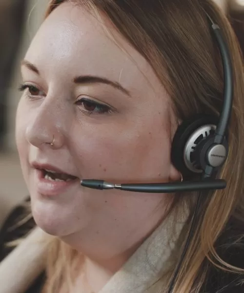 A close up shot of a helpline advisor mid-call, wearing a headset.