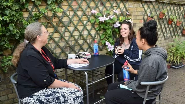 3 women seated at an outdoor table chatting and smiling.