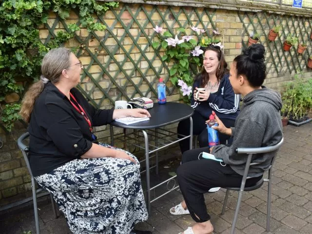 3 women seated at an outdoor table chatting and smiling.