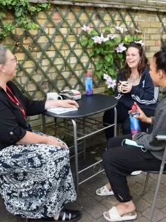 3 women seated at an outdoor table chatting and smiling.