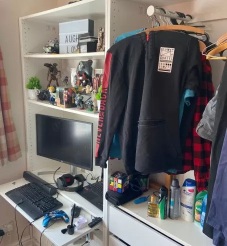 A part of a young person's room, including a small clothing rack, a computer and room decor.