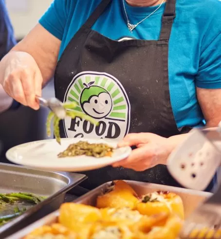 A person with an apron branded with FoodCycle's logo putting some food on a plate.