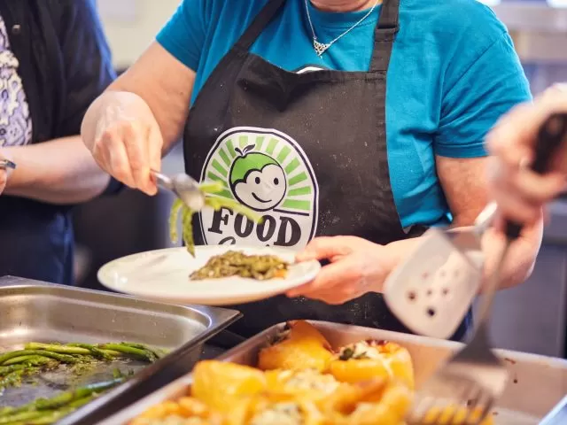 A person with an apron branded with FoodCycle's logo putting some food on a plate.