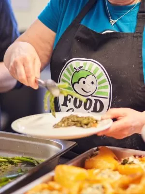 A person with an apron branded with FoodCycle's logo putting some food on a plate.