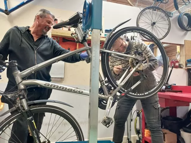 Two people fixing a bike in an indoor workshop.