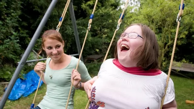 Two people on swings outdoors, smiling and laughing.