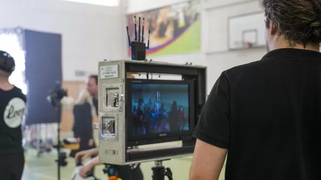 The back of a person watching a performance being recorded, with a screen showing the recording.