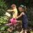 Two children watering plants in a garden with watering cans.