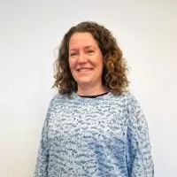 Headshot of Kate Fry in a blue patterned top standing in front of a white background.