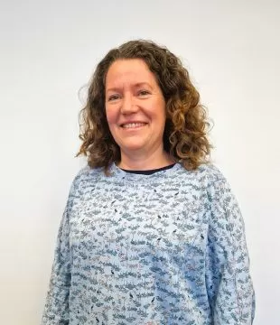 Headshot of Kate Fry in a blue patterned top standing in front of a white background.