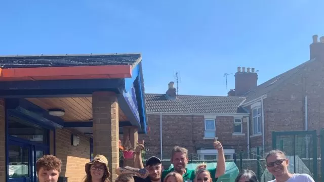 A photo of gardeners, including adults and children, stood outside the Allama Iqbal Centre in Peterborough on a sunny day.