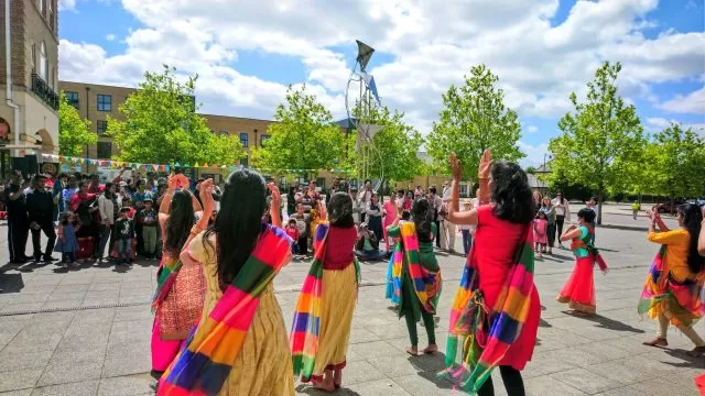 People dressed colourfully dancing outside with a crowd watching.
