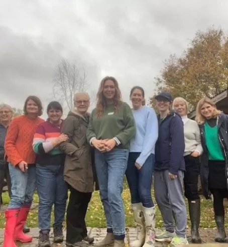 Women gathered together in a line outside in a green space with grey clouds.