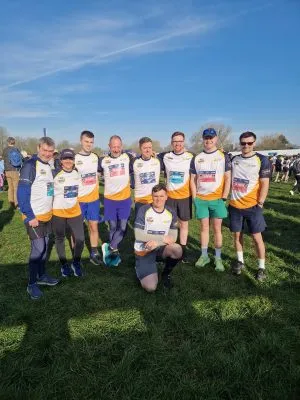 Group of runners standing together with one person crouched in front. They are wearing the same team tops.