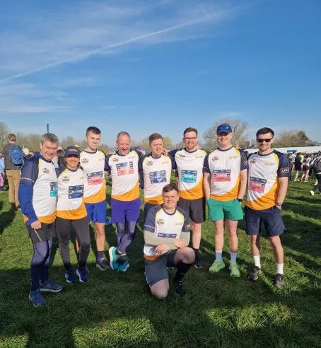 Group of runners standing together with one person crouched in front. They are wearing the same team tops.