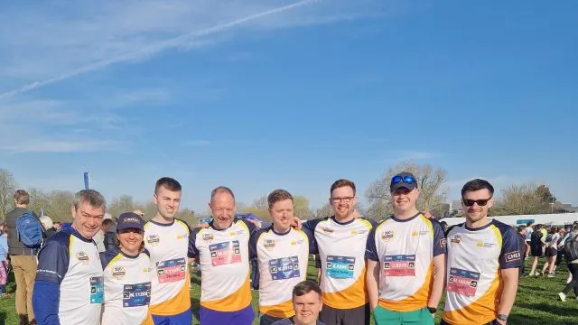 Group of runners standing together with one person crouched in front. They are wearing the same team tops.