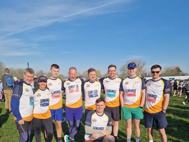 Group of runners standing together with one person crouched in front. They are wearing the same team tops.